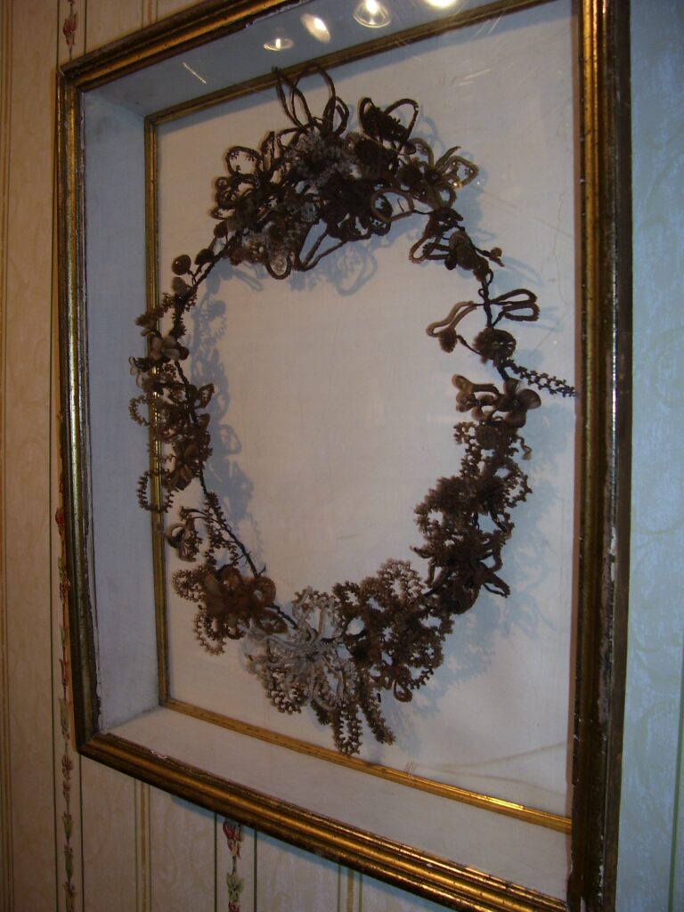 Oval wreath made with mostly brown tones of human hair woven into several different shapes and sizes of flower petals and leaves.